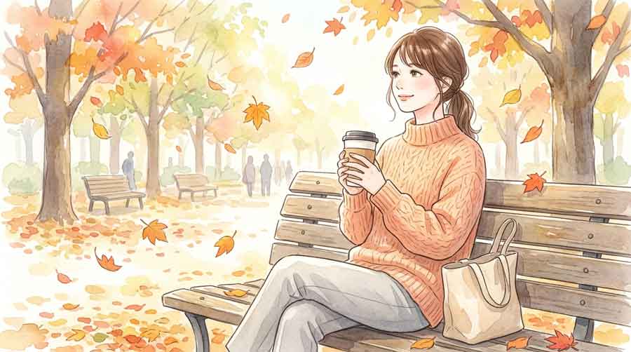 秋の公園のベンチでコーヒーカップを持ちながら穏やかに休息している女性